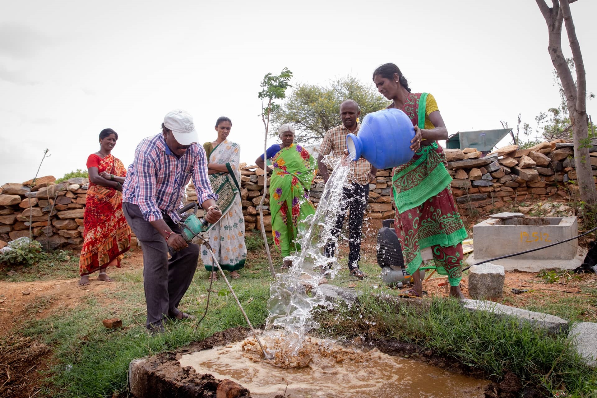 A women pours water into a bio-digester in which cow dung is ground by a man with a cement mixer. 